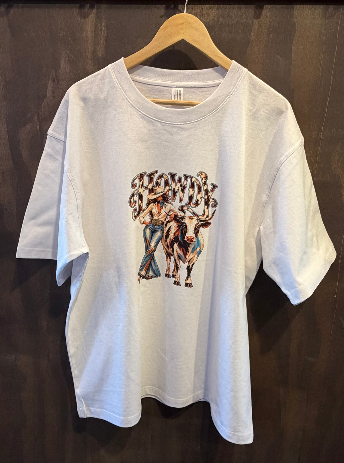 White oversized tee on a hanger with HOWDY cowgirl and longhorn graphic